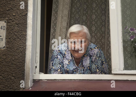 Homebound vieille femme socialise avec les passants dans la fenêtre de son appartement Zielona Gora, Pologne. Banque D'Images