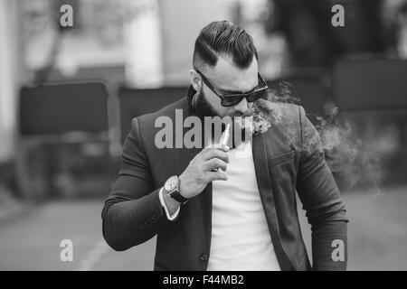 Homme avec une barbe fume cigarette électronique Banque D'Images