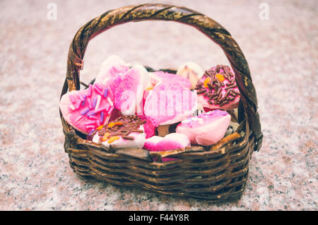 Beau panier poignée incurvée typique assis sur surface de granit rempli de délicieux cookies principalement de couleur rose Banque D'Images