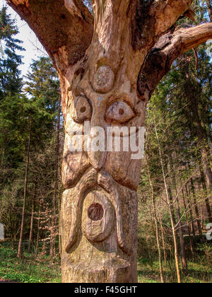 Un tronc d'arbre sculpté avec un drôle de visage décore une forêt en Suisse. Banque D'Images