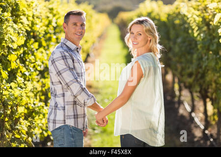 Portrait of smiling couple holding hands and standing next to grapevine Banque D'Images