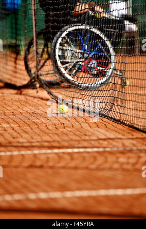 Joueur de tennis en fauteuil roulant non focalisé est vu derrière un filet de tennis sur une cour d'argile Banque D'Images