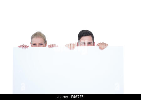 Jeune couple de se cacher derrière un blank sign Banque D'Images