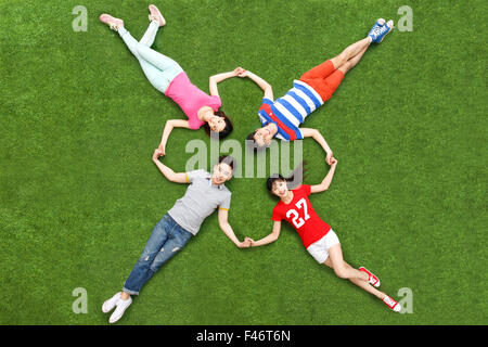 Quatre jeunes gens lying on grass main dans la main Banque D'Images