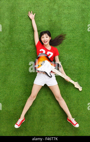 Jeune femme jouant de la guitare sur l'herbe Banque D'Images