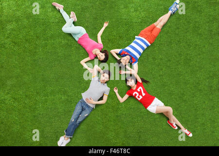 Quatre jeunes gens lying on grass main dans la main Banque D'Images
