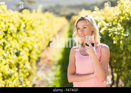 Smiling blonde woman with wineglass en face de grapevine Banque D'Images