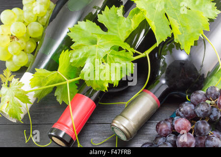 Trois bouteilles de vin et de raisins sur table en bois foncé Banque D'Images