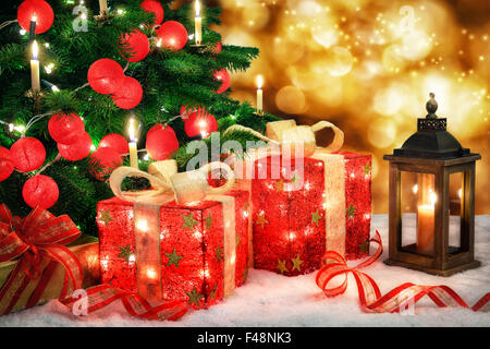 Scène de Noël brillant avec un arbre de Noël illuminé et boules rouges, cadeaux d'ornement avec lampes, une lanterne et de l'effet bokeh Banque D'Images