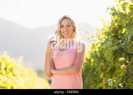 Portrait of smiling blonde woman with wineglass en face de grapevine Banque D'Images