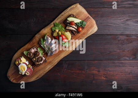 Variété de sandwichs ouverts denses, sombres beurré de pain de seigle avec différentes garnitures. Smorrebrods danois sur toile en bois. Ni Banque D'Images