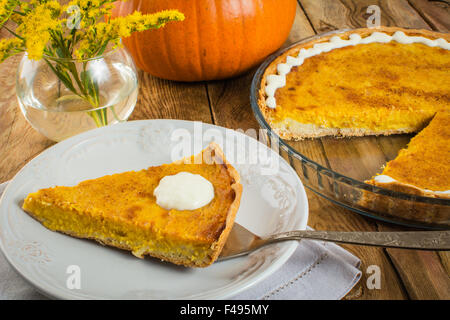 Tarte au potiron Thanksgiving tranche sur plaque blanche, , serviette de table, un plat de cuisson en verre, vase, fleurs jaunes sur un fond de bois Banque D'Images