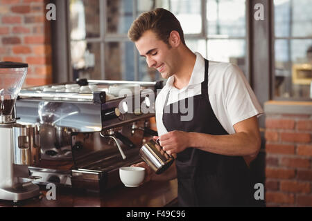 Smiling barista pouring lait en tasse Banque D'Images