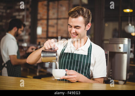 Smiling barista de verser le lait dans une tasse Banque D'Images