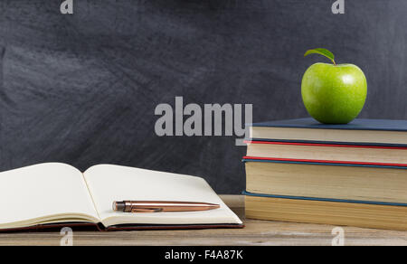 Bureau rustique de l'étudiant, vue en gros, avec des livres, du papier et un stylo ainsi qu'un green apple en avant du tableau. Banque D'Images