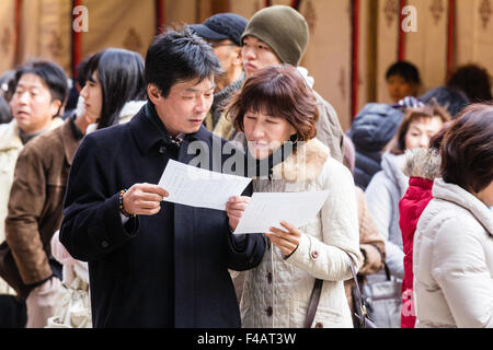 Nishinomiya sanctuaire Shinto du Japon au cours de Shogatsu, nouvelle année. Middle aged couple japonais dans la lecture de leurs manteaux, omikuji, fortune papier, ensemble. Banque D'Images