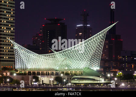 Kobe, Japon. Vue de côté du musée maritime de la mer la nuit, illuminé construit pour ressembler à la coque d'un navire, les blocs de grande hauteur derrière. Banque D'Images