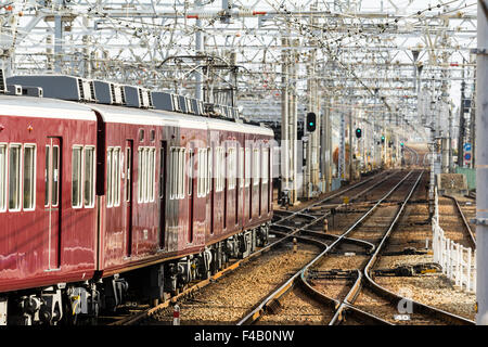 Le Japon. Vue le long labyrinthe de voies de chemin de fer et d'une couleur marron slidings Hankyu Nishinomiya privé train approchant, le jour, la lumière du soleil. Banque D'Images