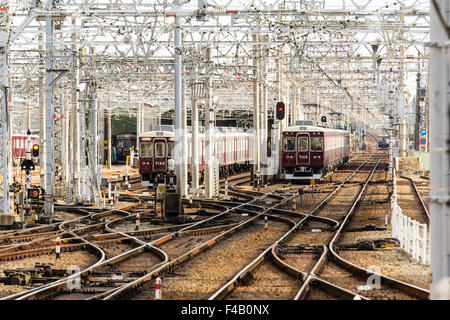 Le Japon. Vue le long labyrinthe de voies de chemin de fer et d'une couleur marron slidings Hankyu Nishinomiya privé train approchant, le jour, la lumière du soleil. Banque D'Images