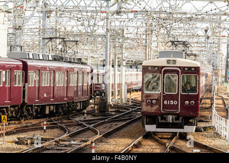 Le Japon. Vue le long labyrinthe de voies de chemin de fer et d'une couleur marron slidings Hankyu Nishinomiya privé train approchant, le jour, la lumière du soleil. Banque D'Images