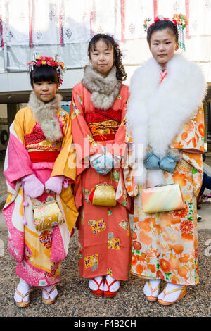 Le Japon, Nishinomiya culte. Trois enfants, soeurs, posant dans une ligne de court-circuit à haute, portant des kimono et transportant des sacs à main de cérémonie. Eye-contact. Banque D'Images