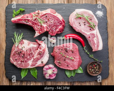 Steaks de viande crue aux épices sur la planche à découper noire. Banque D'Images