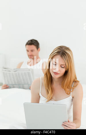 La femme est sur son ordinateur portable pendant que son mari est reading newspaper Banque D'Images