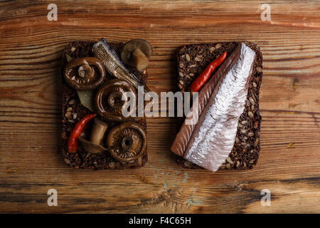 Deux différents sandwichs ouverts de dense de farine de seigle Pain (rugbrod) avec champignons marinés du sauvage, anchois et herrring sur âgés de Banque D'Images