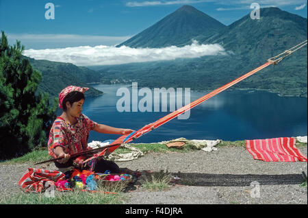 Une jeune fille Maya en costume national tisse à l'aide de son métier tout en surplombant le lac Atitlan au Guatemala. Entouré de volcans, le lac Atitlan est le plus grand plan d'eau en Amérique centrale (1 120 341 pieds/mètres) et considéré comme l'un des plus beaux lacs du monde. Banque D'Images