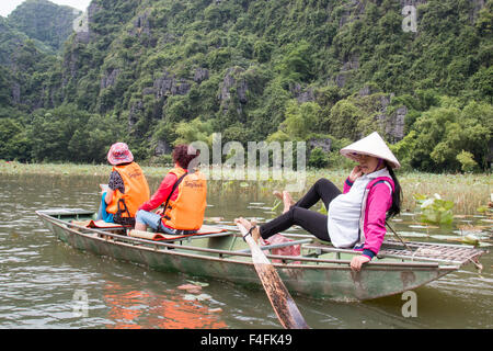 Dame vietnamienne enceinte lignes avec ses pieds deux touristes japonais en gilets le long de la rivière ngo dong,Tam Coc, Ninh Binh Banque D'Images