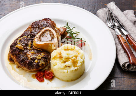 Les plats osso buco de veau avec les tomates et la purée de pomme de terre sur la plaque blanche sur fond de bois Banque D'Images