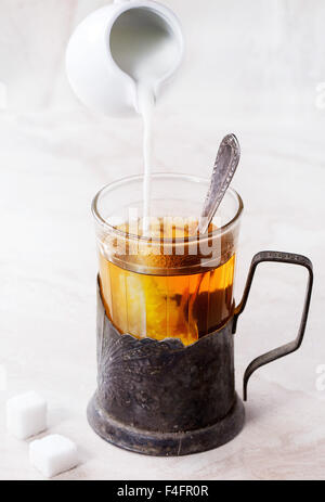 Verser le lait de blanc de jug retro tasse de thé en verre vintage avec cuillère à café et des morceaux de sucre sur le marbre blanc bac Banque D'Images