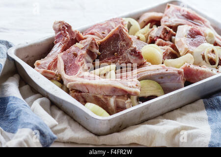 Faire mariner les côtelettes d'agneau de matières premières avec l'oignon, l'huile d'olive et le poivre dans un plat de cuisson en aluminium anciens sur table de cuisine blanche avec poupée russe Banque D'Images