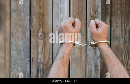 Arrestation, close-up shot man's hands avec des menottes en face du mur de bois en planches avec copy-space Banque D'Images