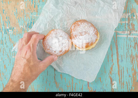 Main mâle atteint et picking sweet donut sucré à partir de la table de cuisine en bois rustique, classique hannukah sufganiyot boulangerie savoureux ou d Banque D'Images