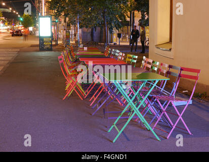 Une rangée de tables et chaises de couleur vive à l'extérieur d'un café à Helsinki, Finlande la nuit. Banque D'Images