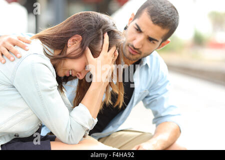 Vue latérale d'un musulman réconfortant un triste caucasian girl deuil dans une gare Banque D'Images