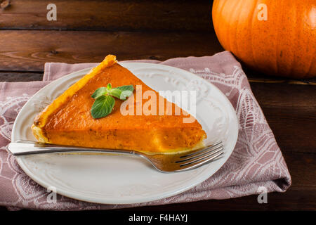 Un morceau de tarte à la citrouille avec de la menthe, plaque blanche, fourche, , serviette sur fond de bois foncé Banque D'Images