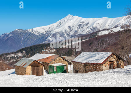 Maisons rurales en pierre sur pente enneigée et montagnes couvertes de neige sur contexte en Piémont, Italie du Nord. Banque D'Images