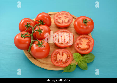 - Couper les tomates, ensemble et sur la vigne d'un bouquet de basilic frais sur une planche en bois Banque D'Images