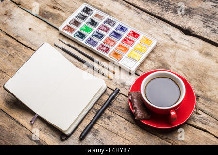 Ordinateur portable ouvert avec les peintures à l'aquarelle et tasse de café sur la table en bois. Vue d'angle de la maquette artistique Banque D'Images