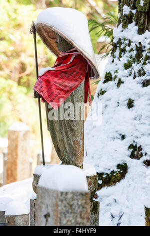 Le Japon, Koyasan, Okunoin cemetery. Prêtre de la pierre couverte de neige rouge statue bouddhique, soumission et chapeau conique, et la tenue du personnel. L'hiver Banque D'Images