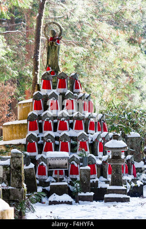 Le Japon, Koyasan, Okunoin cemetery. La neige a couvert les petits rouges-bibbed statues jizo-bosatsu empilées en pyramide avec grande statue bosatsu sur le dessus. Banque D'Images