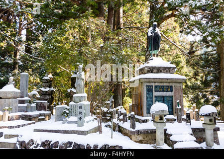 Koyasan, Japon, cimetière Okunoin, hiver, neige. Divers monuments en pierre, des pierres tombales, et des lanternes à piédestal le dégagement en forêt de cèdres. Banque D'Images