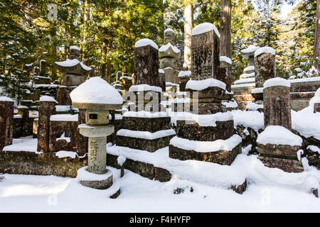 Koyasan, Japon, cimetière Okunoin, hiver, neige. Divers monuments en pierre, des pierres tombales, et des lanternes à piédestal le dégagement en forêt de cèdres. Banque D'Images