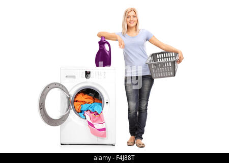 Portrait d'une jeune femme tenant un panier vide et s'appuyant sur une lessive au-dessus d'un lave-linge Banque D'Images