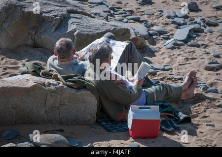 Un couple dans la soixantaine de lire sur une plage à Cornwall Banque D'Images