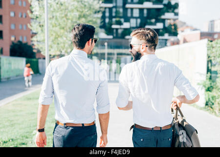 La figure du genou de deux jeunes blonds barbus et les cheveux noirs d'affaires moderne, marcher dans la ville de rétro-éclairage, voir de l'arrière - travail, concept à succès Banque D'Images