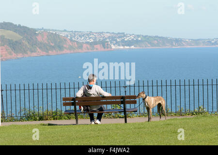 Homme assis sur un banc avec Greyhound dog surplombant Torbay de Babbacombe Downs, Devon, Angleterre Banque D'Images