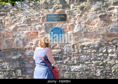 Femme lisant English Heritage Blue Plaque - 'dramaturge Oscar Wilde a résidé à Babbacombe Cliff' signe à Torquay, Devon, Angleterre Banque D'Images